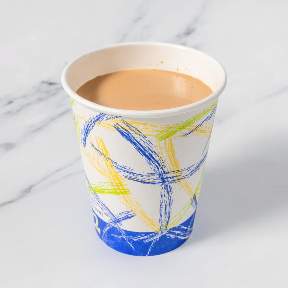 Paper cup with colorful blue, yellow, and green brushstroke designs filled with a light brown beverage on a marble surface.
