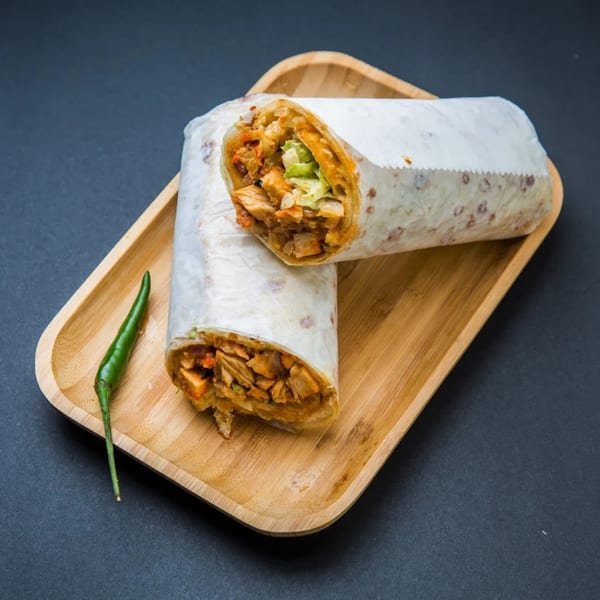 Two Indian chicken wraps with lettuce and sauce on a wooden tray with a green chili.