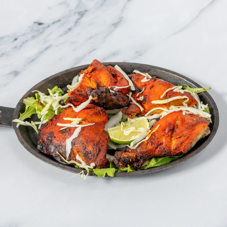 Char-grilled tandoori chicken pieces arranged on lettuce with shredded cabbage and a lime wedge.