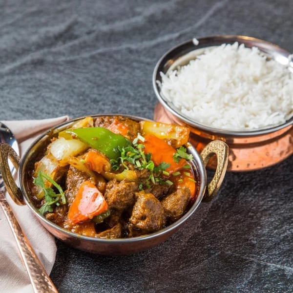 Indian lamb curry with bell peppers and onions, served with white rice in copper bowls.