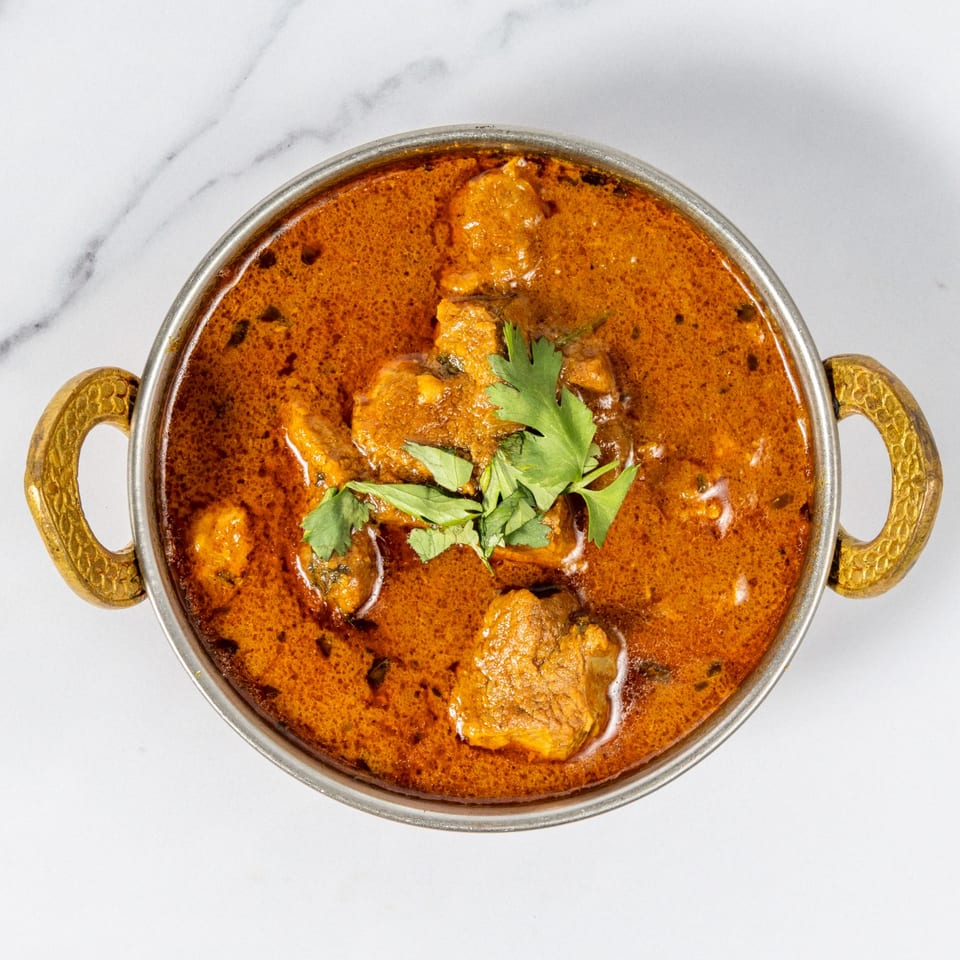 Overhead view of chicken curry in a brass-handled bowl, garnished with fresh cilantro on a white marble surface.