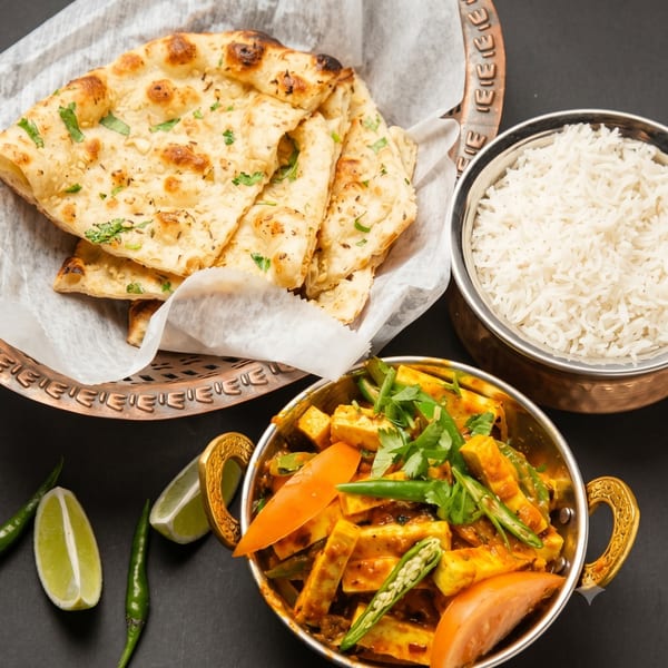 Indian meal with naan bread, white rice, and paneer curry with vegetables and lime wedges.