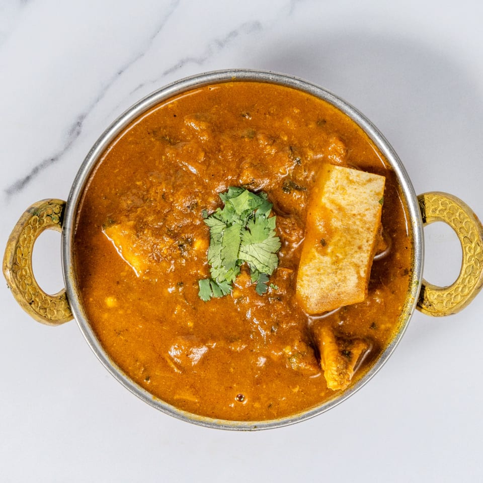 Indian curry with tender pieces, fresh cilantro, and a crisp pastry served in an ornate handled bowl.