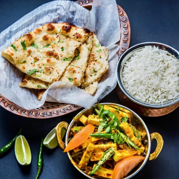 Indian meal with naan bread, white rice, and paneer curry in copper bowls, garnished with lime and chilies.